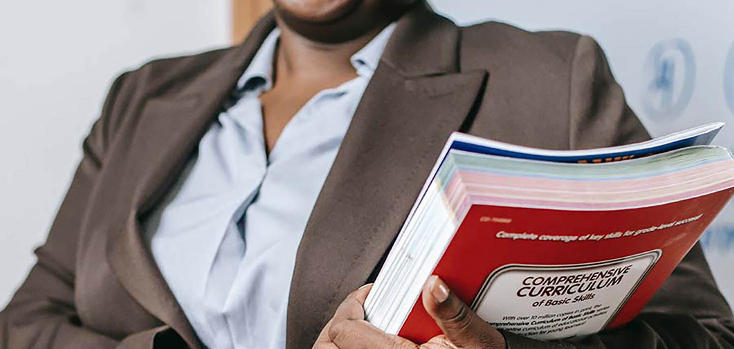 A woman holds a book that is labelled “Comprehensive Curriculum.”