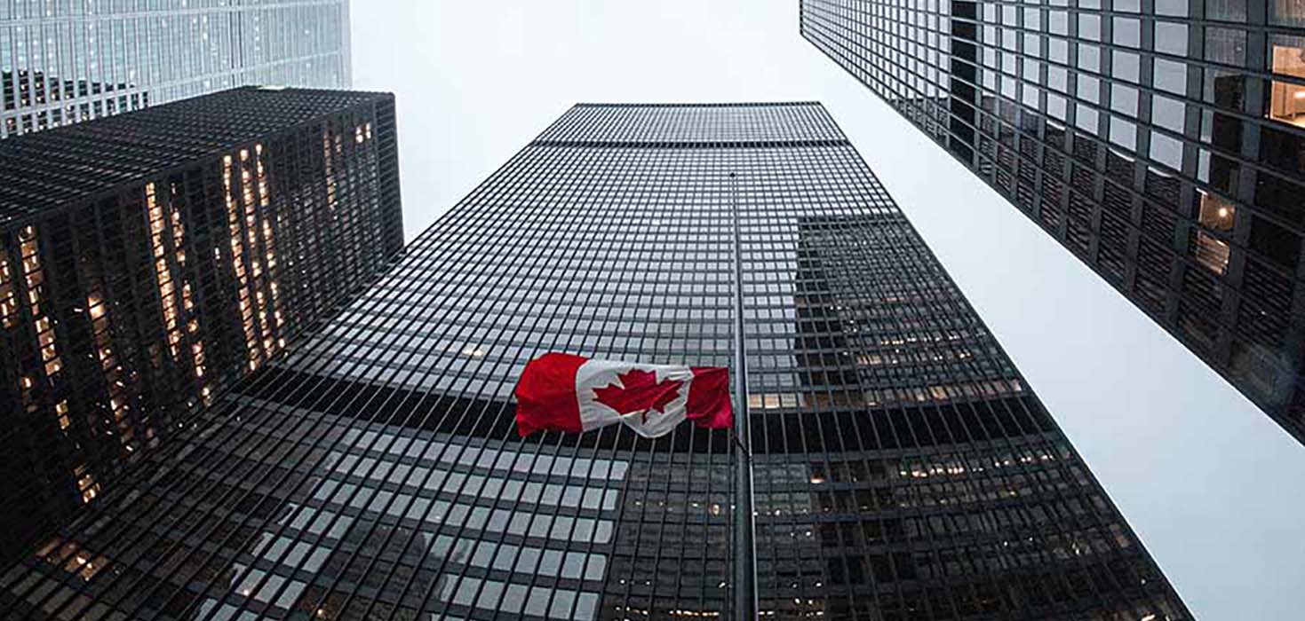 Several skyscrapers loom tall as a Canadian flag flaps between them.