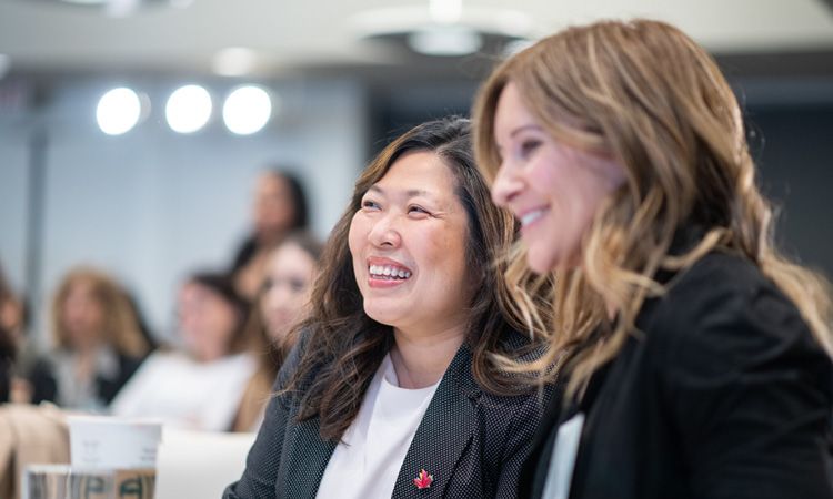 Two women smile while attending a conference.