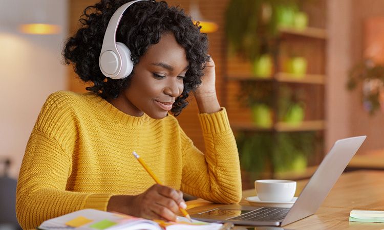 Woman with headphones on working on laptop and taking notes.