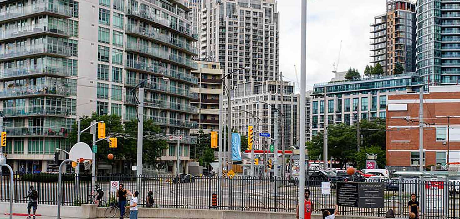 A busy urban neighbourhood with a busy basketball court in the foreground and tall condos in the background.