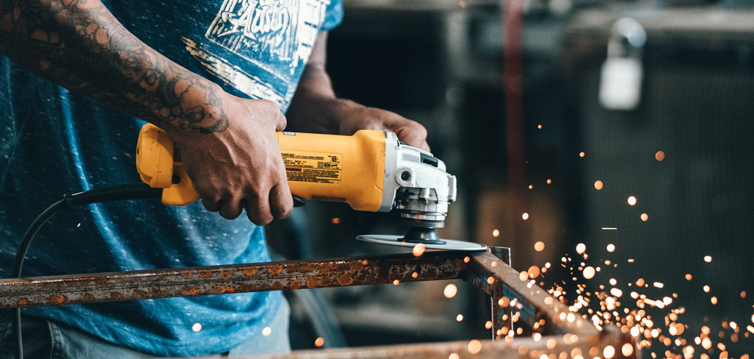 Worker uses power tool to cut cylindrical material. 