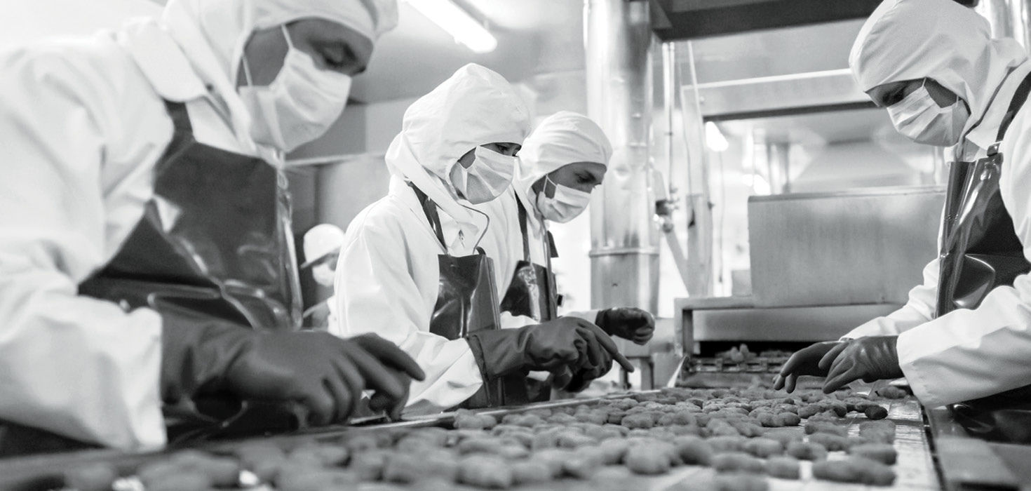 Several workers on a factory line inspect goods on a conveyor belt.