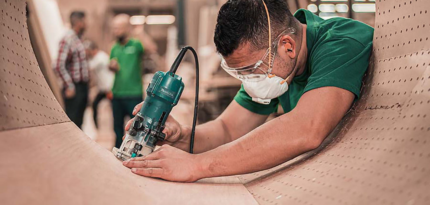 Young worker uses power tool to cut cylindrical material. 