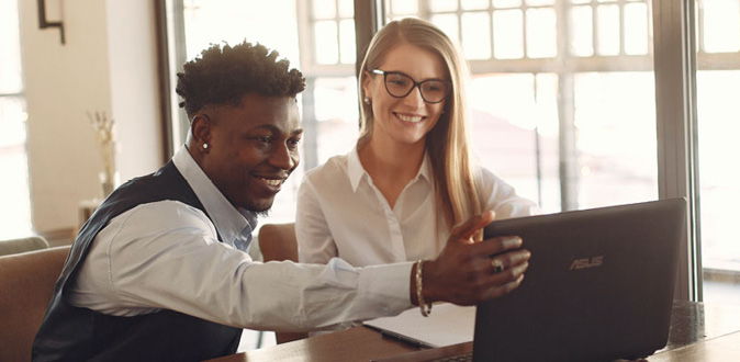 Man and woman sitting at table, smiling and looking at the computer screen. 