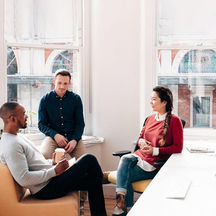 Three coworkers sitting and talking in a bright office.