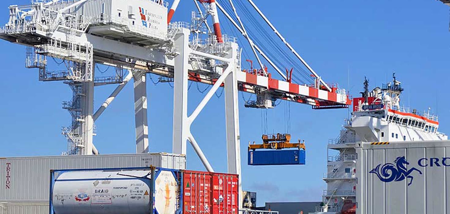 A tower of shipping containers being loaded onto a ship on a sunny day.