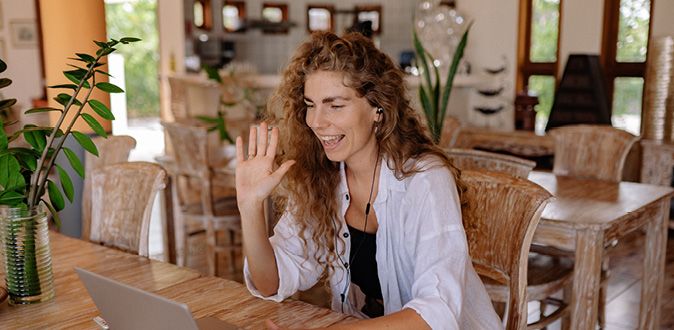 Woman sitting at a table waving at the computer.